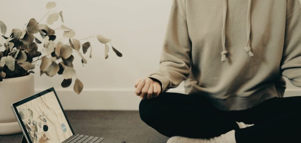 Woman practicing meditation next to a laptop