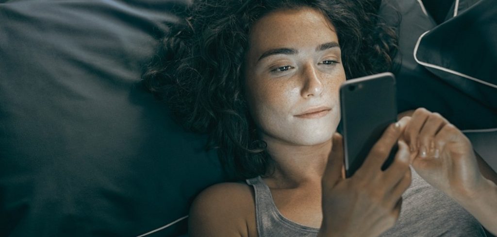 Woman overthinking at night looking at her smartphone in bed