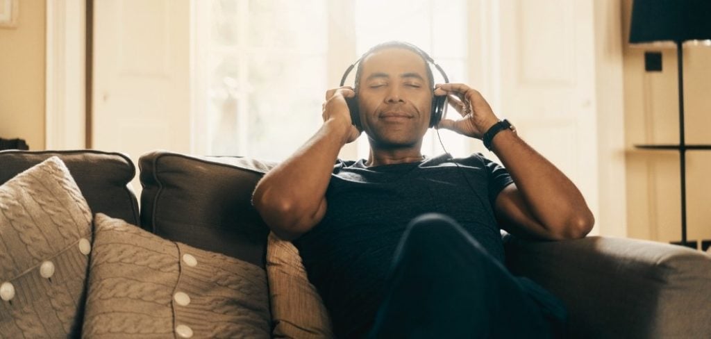Man listening to music mindfully on the couch with headphones on smiling
