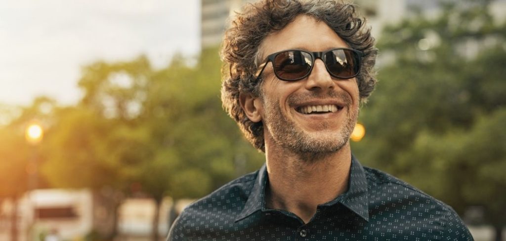 A man smiling happily outside in the sunshine with sunglasses on