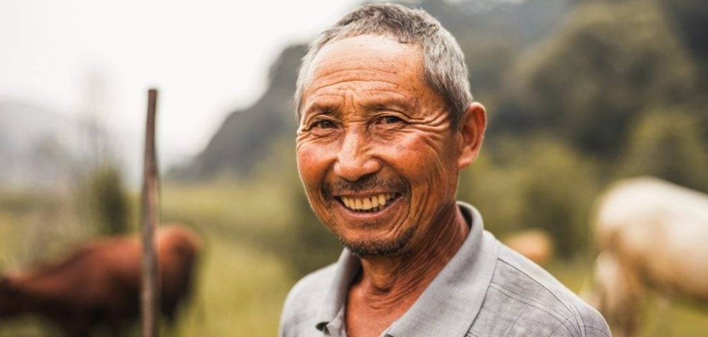 Farmer smiling in front of a field of cows with a mountain in the background