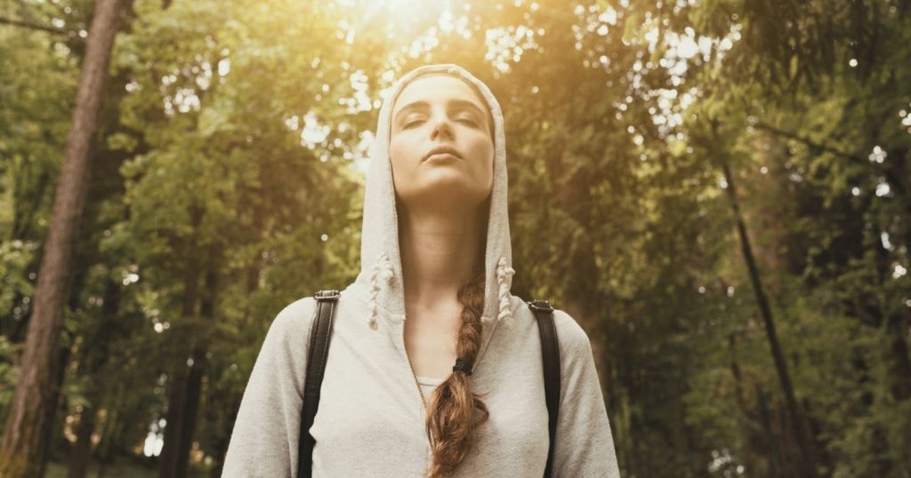A teenager hiking in the forest experiencing mindfulness with her eyes closed observing the environment