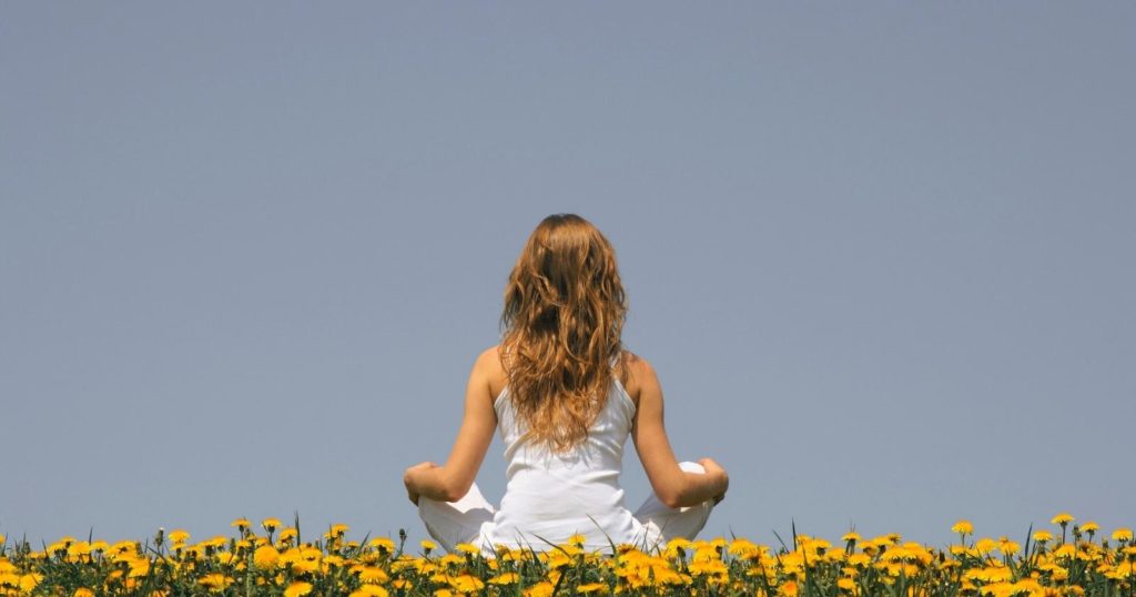 Woman sitting in field of yellow flowers practicing mindfulness exercises