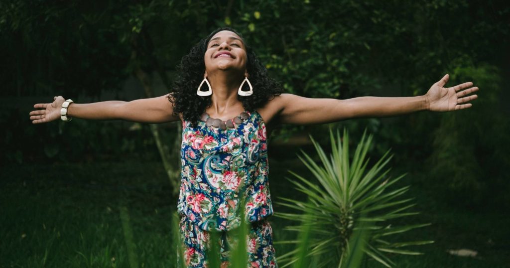 Woman expressing gratitude with her arms open in front of a lush green background