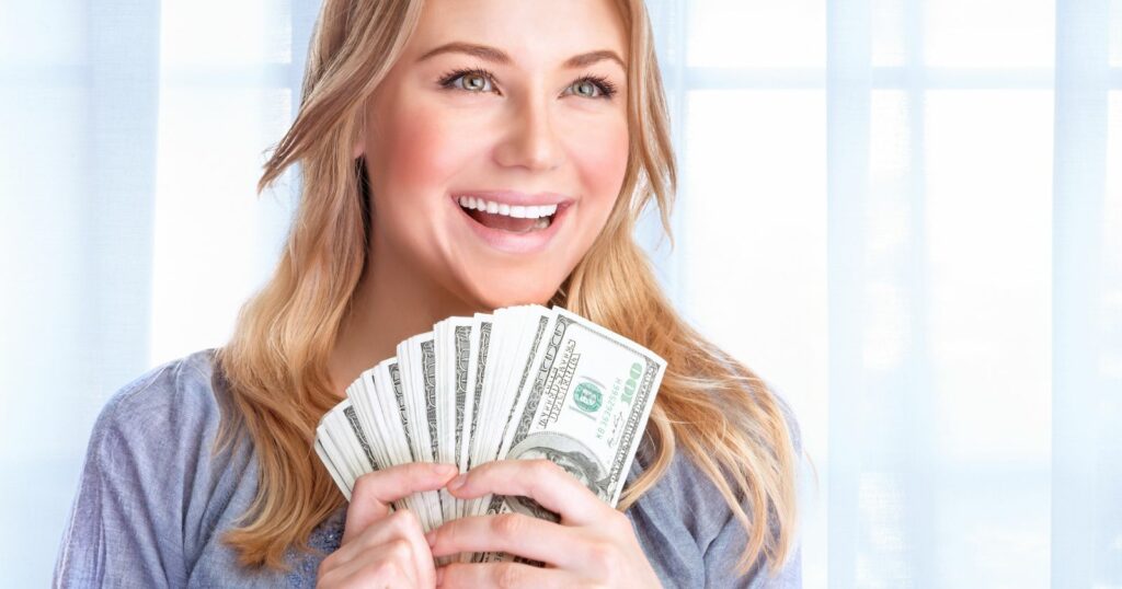 A smiling woman holding a stack of hundred dollar bills.